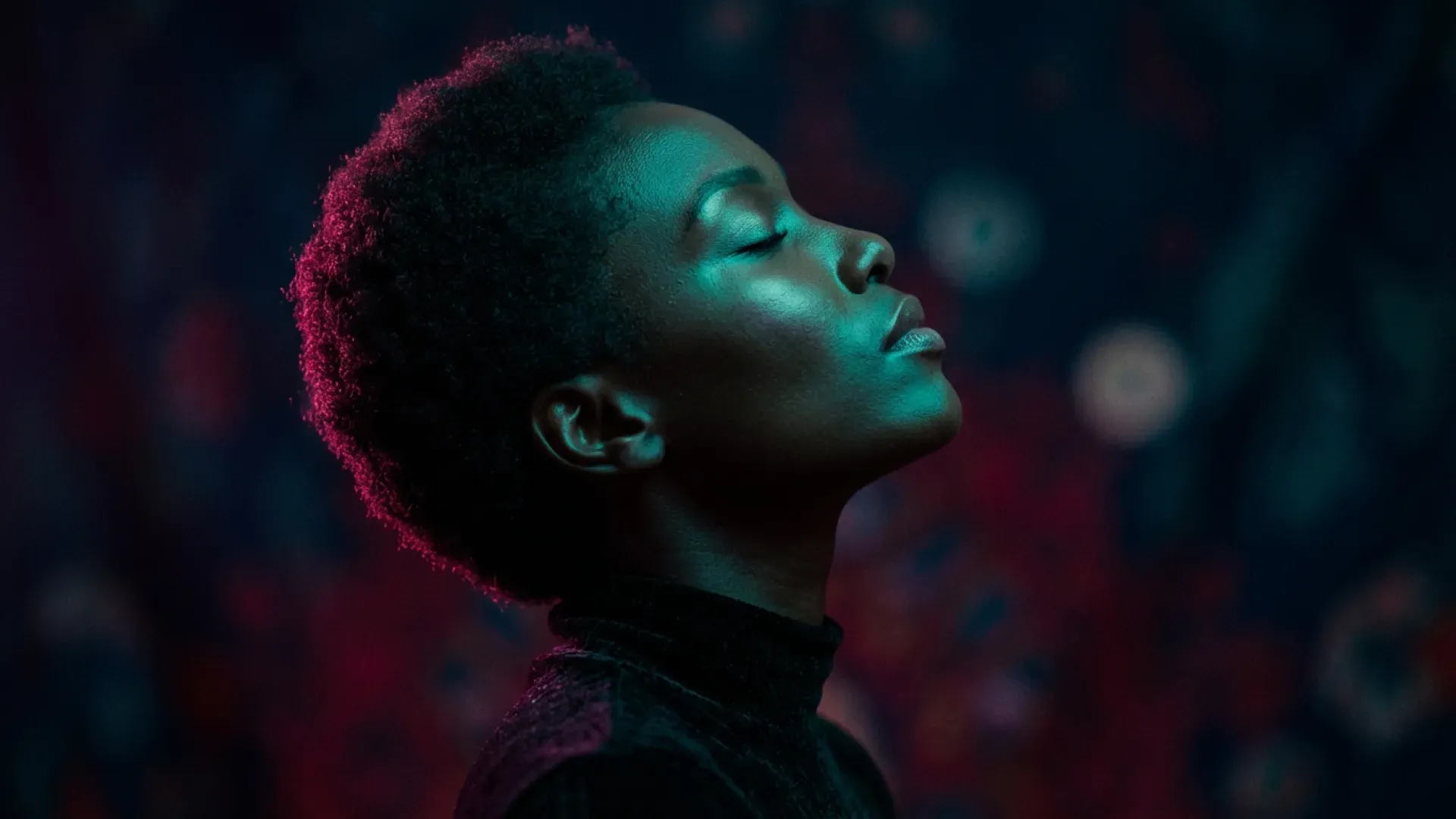 Side-profile portrait lit by teal and magenta light against a dark background